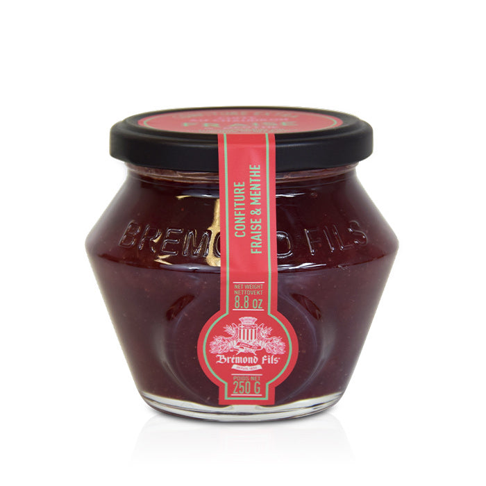 Un pot en verre contenant de la confiture de fraise et menthe de la marque Bremond Fils. Le couvercle est noir et l'étiquette rouge indique 'Confiture fraise & menthe' avec un poids net de 250 g. La confiture a une couleur rouge foncé, montrant sa texture lisse et appétissante.