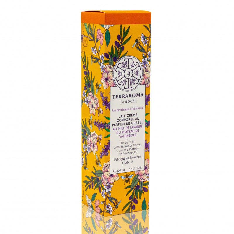 Boîte de lait crème corporel au parfum de grasse, contenant 200 ml. L'emballage est de couleur orange avec des motifs floraux colorés, mettant en avant le miel de lavande du plateau de Valensole. L'étiquette indique que le produit est fabriqué en Provence.