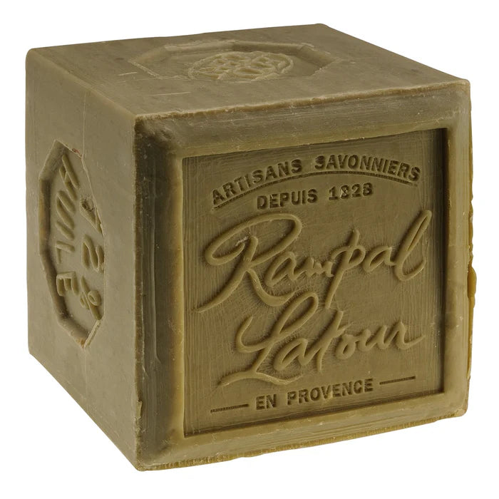 Un savon artisanal de la marque Rampal Latour, fabriqué à l'huile d'olive. Le savon se présente sous la forme d'un cube de couleur verte, avec le logo de la marque et des inscriptions indiquant son origine artisanale et son année de fondation (1928). Le savon est marqué de la mention 'en Provence' et présente une texture naturelle.