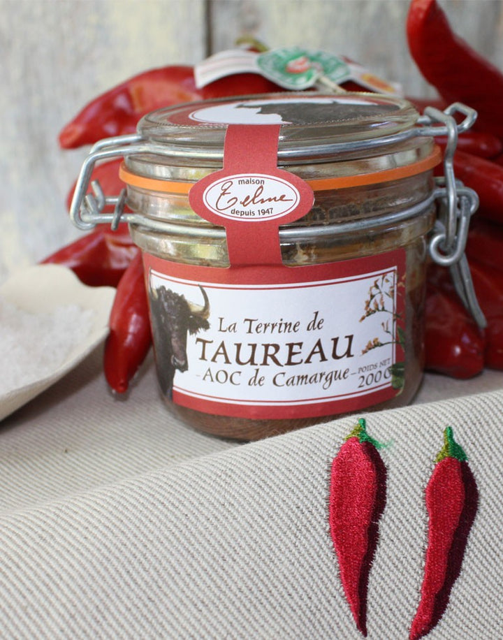 Terrine de Taureau AOC de Camargue, présentée dans un pot en verre avec une étiquette de la Maison Telme, depuis 1947. Le pot est entouré de poivrons rouges et de décorations rappelant la Provence, évoquant les saveurs authentiques et le caractère régional de cette spécialité.