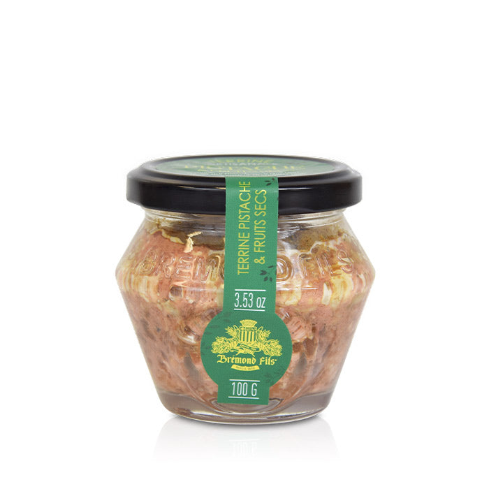 Un petit pot en verre de terrine à la pistache et aux fruits secs, de la marque Bremond Fils. Le pot a un couvercle noir avec une étiquette verte indiquant le nom du produit et son poids de 100 g (3.53 oz). À travers le verre, on peut voir la texture de la terrine avec des couleurs brunâtres et dorées.